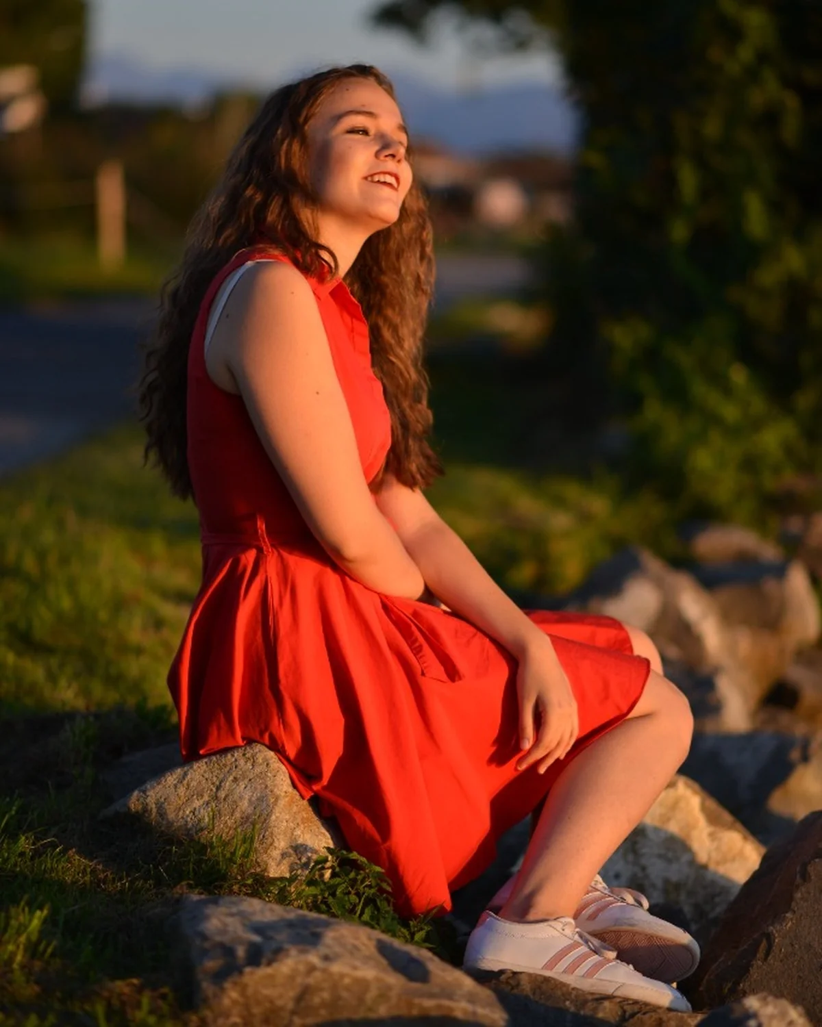 Porträt im roten Kleid sitzend auf Ufersteinen in Abendsonne