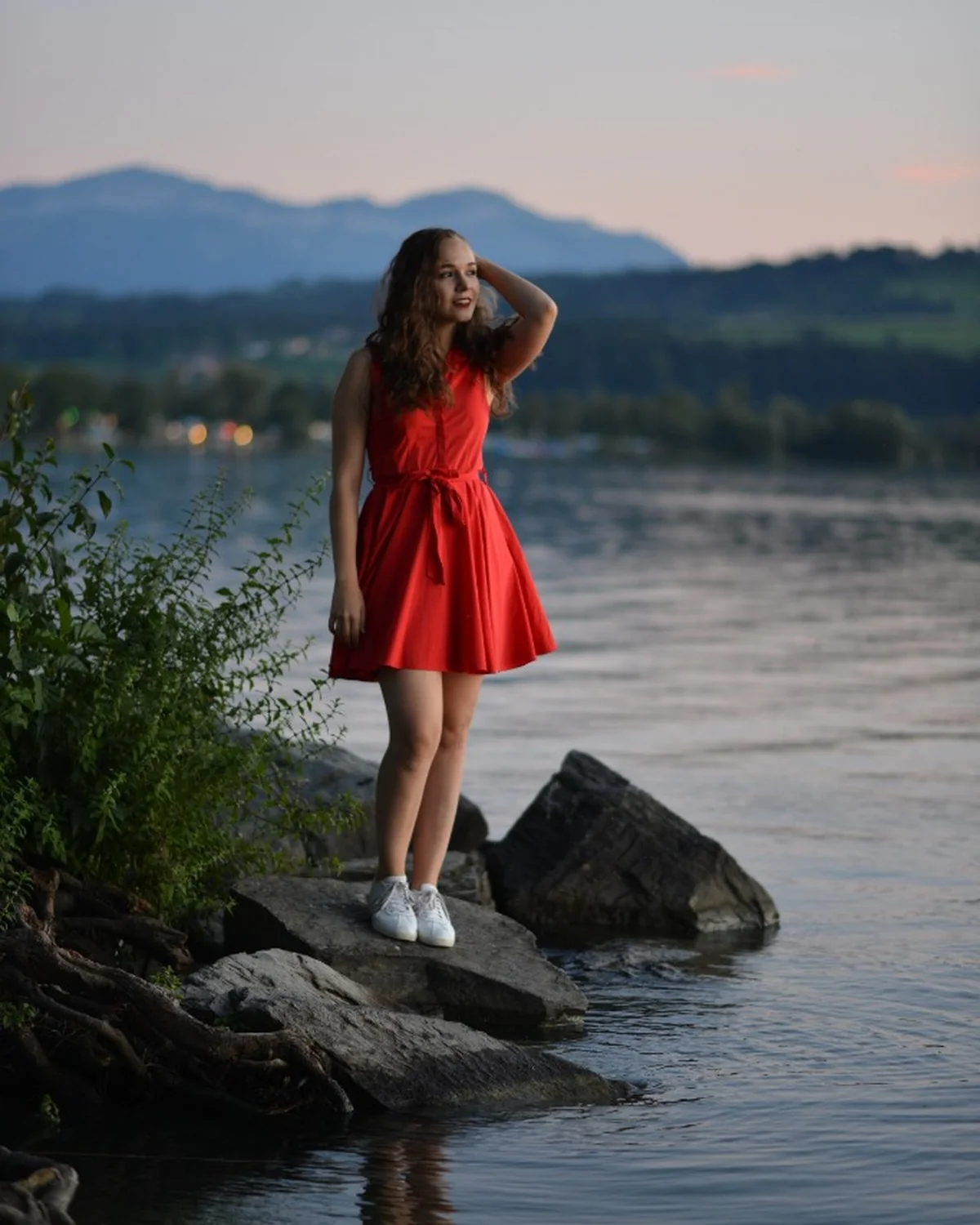 Porträt im roten Kleid stehend auf Uferfelsen in blauer Stunde